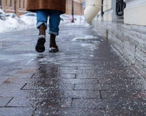 Selective focus on technical salt grains on icy sidewalk surface in wintertime, used for melting ice and snow. Applying salt to keep roads clear and people safe in winter weather from ice or snow